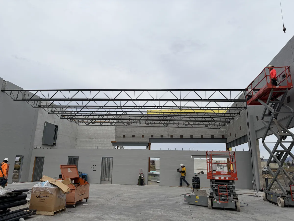 Steel roof joists set across the masonry walls of the new Discount Tire building, crews on scissor lifts