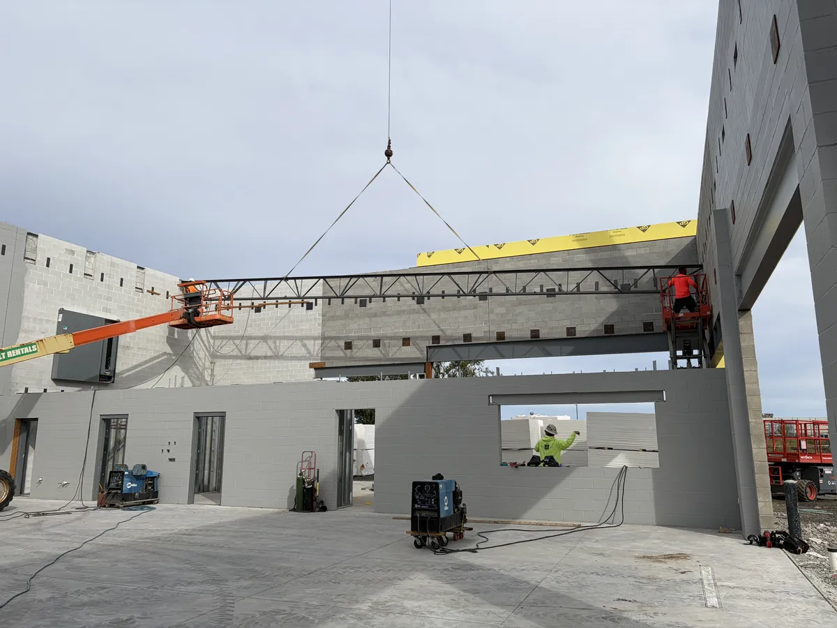 A steel joist lowered into place by crane while the crew guides it from lifts